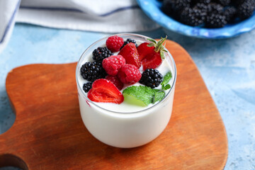 Glass of tasty yogurt with different fresh berries and mint on light blue background