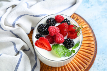 Glass of tasty yogurt with different fresh berries and mint on light blue background