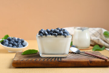 Glass bowl of tasty yogurt with fresh blueberries on brown background