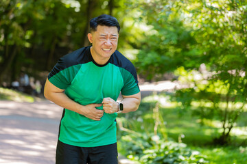 Middle-aged Asian runner feeling sudden strong abdominal stomach ache, gastritis problem outdoors in park. Man in sportswear having symptom poisoning diarrhea indigestion peptic ulcer pancreatitis
