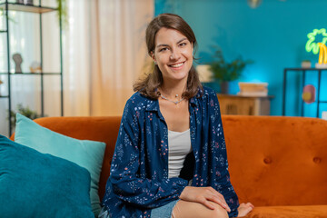 Portrait of happy calm Caucasian woman at home couch smiling friendly, glad expression looking at camera resting, relaxation feel satisfied good news, celebrate win. Smiling young girl in living room.