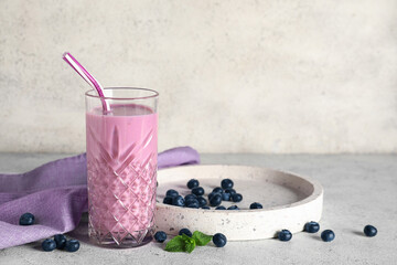 Glass of fresh blueberry smoothie and plate with berries on white background