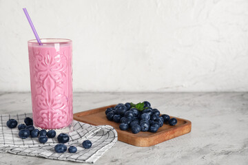 Glass of fresh blueberry smoothie and wooden board with berries on white background
