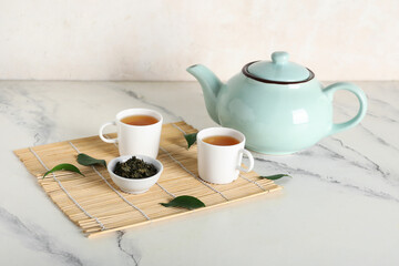 Cups and teapot of hot tea with dried leaves on white background