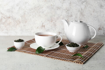 Cup and teapot of hot tea with dried leaves on white background