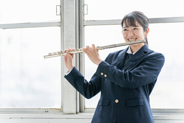 教室でフルートを吹く吹奏楽部のアジア人女子高生  © buritora