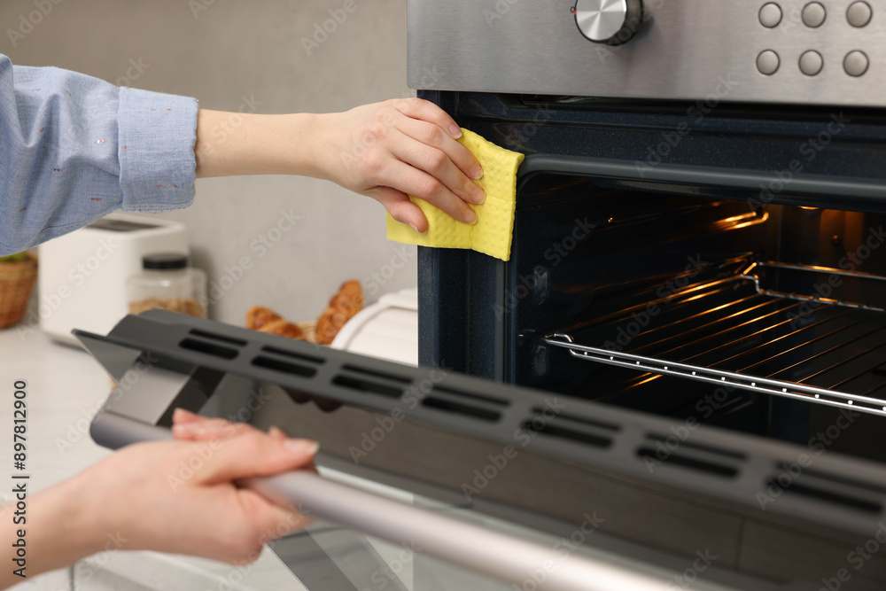 Wall mural Woman cleaning electric oven with rag in kitchen, closeup