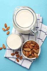 Glass of almond milk, jug and almonds on light blue wooden table, top view