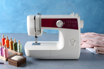 White sewing machine and craft accessories on gray table near light blue wall