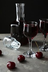 Delicious cherry liqueur in glasses, decanter and fresh berries on grey table