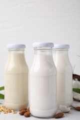 Different types of vegan milk in bottles and ingredients on white tiled table, closeup