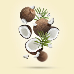 Coconuts and green leaves falling on beige background