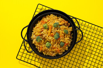 Pilaf in frying pan on grid on yellow background, top view