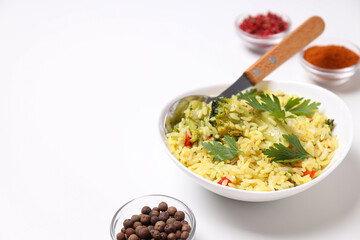 Pilaf in bowl, spices, spoon on white background, space for text