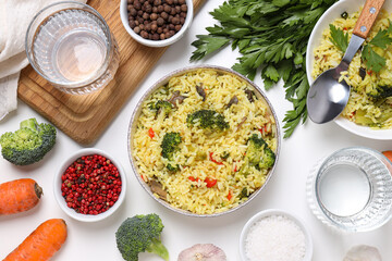 Pilaf, spices, vegetables and glasses of water on white background, top view
