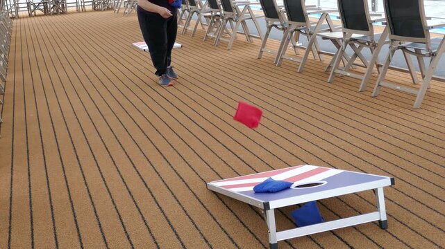 Woman throwing bean bags at USA colors cornhole game on cruise ship deck