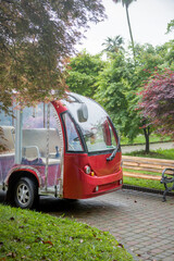 A small red electric tour bus is waiting for passengers on a rainy day in the botanical garden