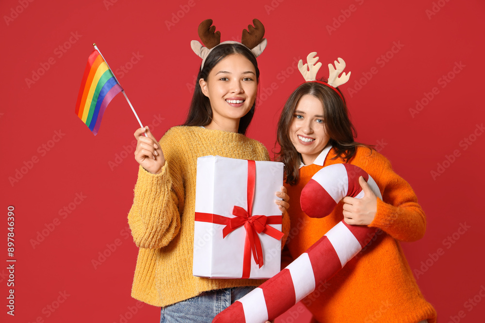 Poster Young lesbian couple with LGBT flag, Christmas gift and candy cane pillow on red background