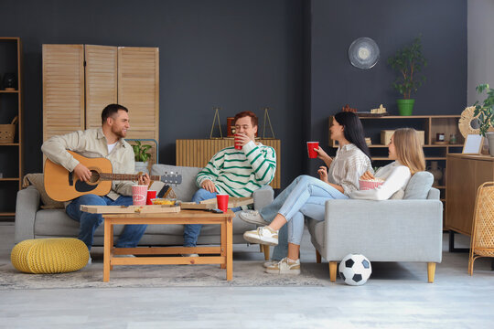 Young man with his friends playing guitar at home party