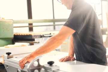 Carpenter working on wood plank using sawing machine in workshop