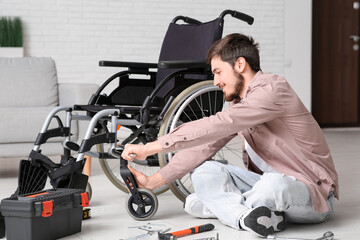 Obraz premium Young man with wrench repairing wheelchair at home