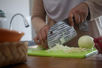 Asian muslim woman peeling, cutting and slicing onion and garlic. Preparing marinade for chicken meat