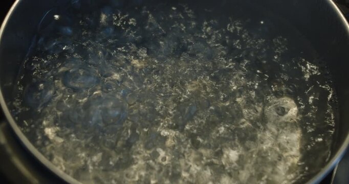 Beautiful close up slow motion shot of a pot of boiling water on the stove with lots of boiling as bubbles form.