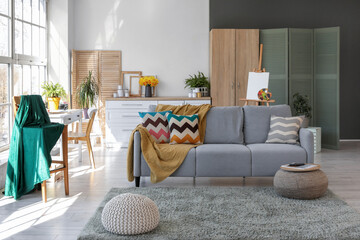 Comfortable sofa with plaid and cushions in interior of living room