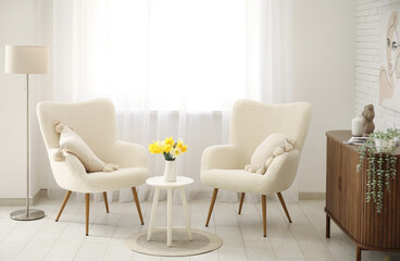 Comfortable armchairs and coffee table with daffodil flowers in interior of living room