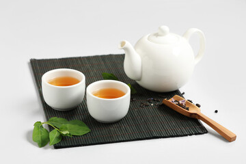 Teapot with cups, wooden scoop of dry tea and leaves on white background
