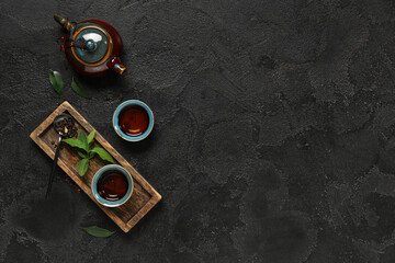 Teapot with cups, spoon of dry tea and leaves on black grunge background