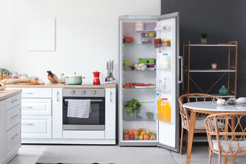 Open fridge full of fresh food near white wall in kitchen