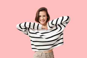 Happy young woman in stylish striped sweater on pink background