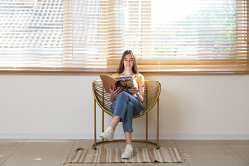 Young woman reading magazine while sitting in armchair in living room