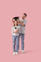 Father putting mortar board on his daughter with piggy bank on pink background. Tuition fees concept