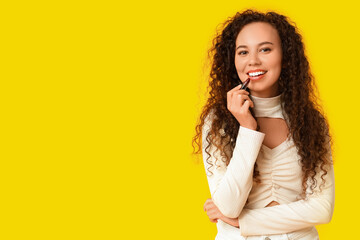 Beautiful young happy African-American woman with lipstick on yellow background