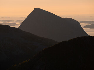 Silhouette of coastal northern Norwegian moutains against the setting and rising midnight sun at...
