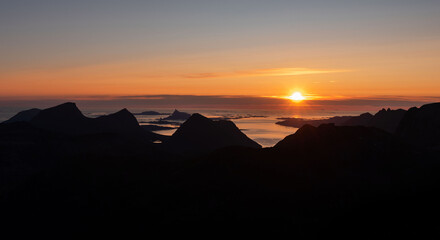 Silhouette of coastal northern Norwegian moutains against the setting and rising midnight sun at dusk and dawn. Dramatic colours and contrast, sun over arctic ocean and mountain ridges