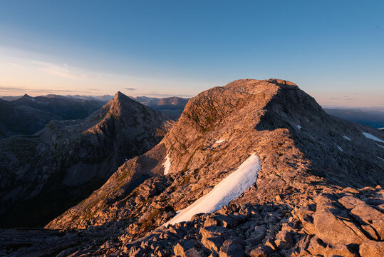 Sunset and blue hour midnight sun view from Tortenviktind, Helgeland, Norway. Arctic night of hiking in Norwegian fjell. Small alpine lakes and pieces of snow in summer hiking, Nordnorge. 