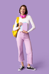 Beautiful female student with headphones, backpack and books on lilac background