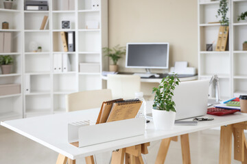 Interior of stylish office with workplaces, laptop and shelving unit