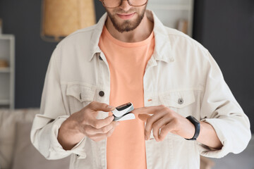 Young man with pulse oximeter at home, closeup