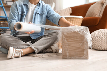 Fototapeta premium Young man wrapping box with stretch film at home, closeup