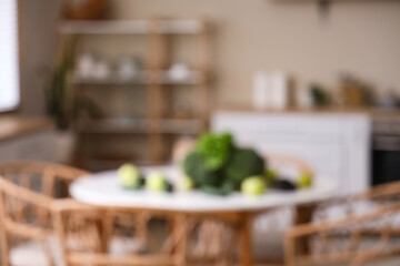 Different fresh green vegetables and fruits on table in kitchen, blurred view
