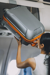 Fototapeta premium Young Female Tourist Storing Luggage in Overhead Compartment on Airplane During Travel