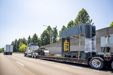 Black and white classic big rig semi truck tractor transporting fastened heavy duty cargo on step...