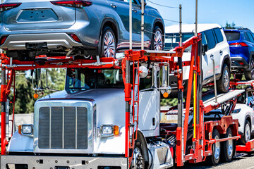 Powerful white car hauler industrial grade big rig semi truck transporting cars and crossovers on...