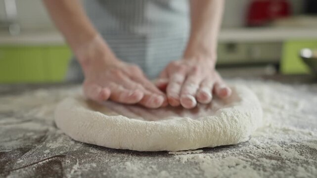 A female chef is kneading dough with her hands in the kitchen for making homemade pizza.
