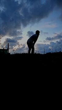 Silhouettes of young men playing cricket in a park in Odisha, India, Vertical Orientation, Slow motion.