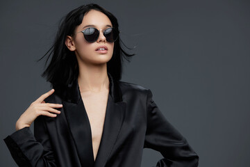Photo of a beautiful asian woman in a black suit and sunglasses, posing against a gray background in a studio, closeup shot, exuding confidence and elegance